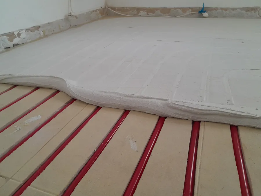 Red heating pipe laid across a floor with insulation board covering part of the room