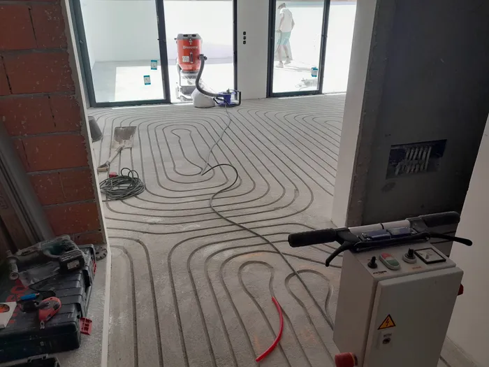Wide shot of a spiral pipe circuit laid across a new-build floor, dust extraction running